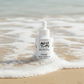 AVYI PRETTY PRIME FACE SERUM bottle on a beach with ocean waves.